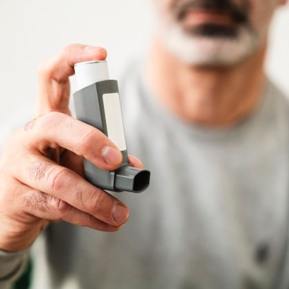 Close up of a man holding a grey asthma inhaler